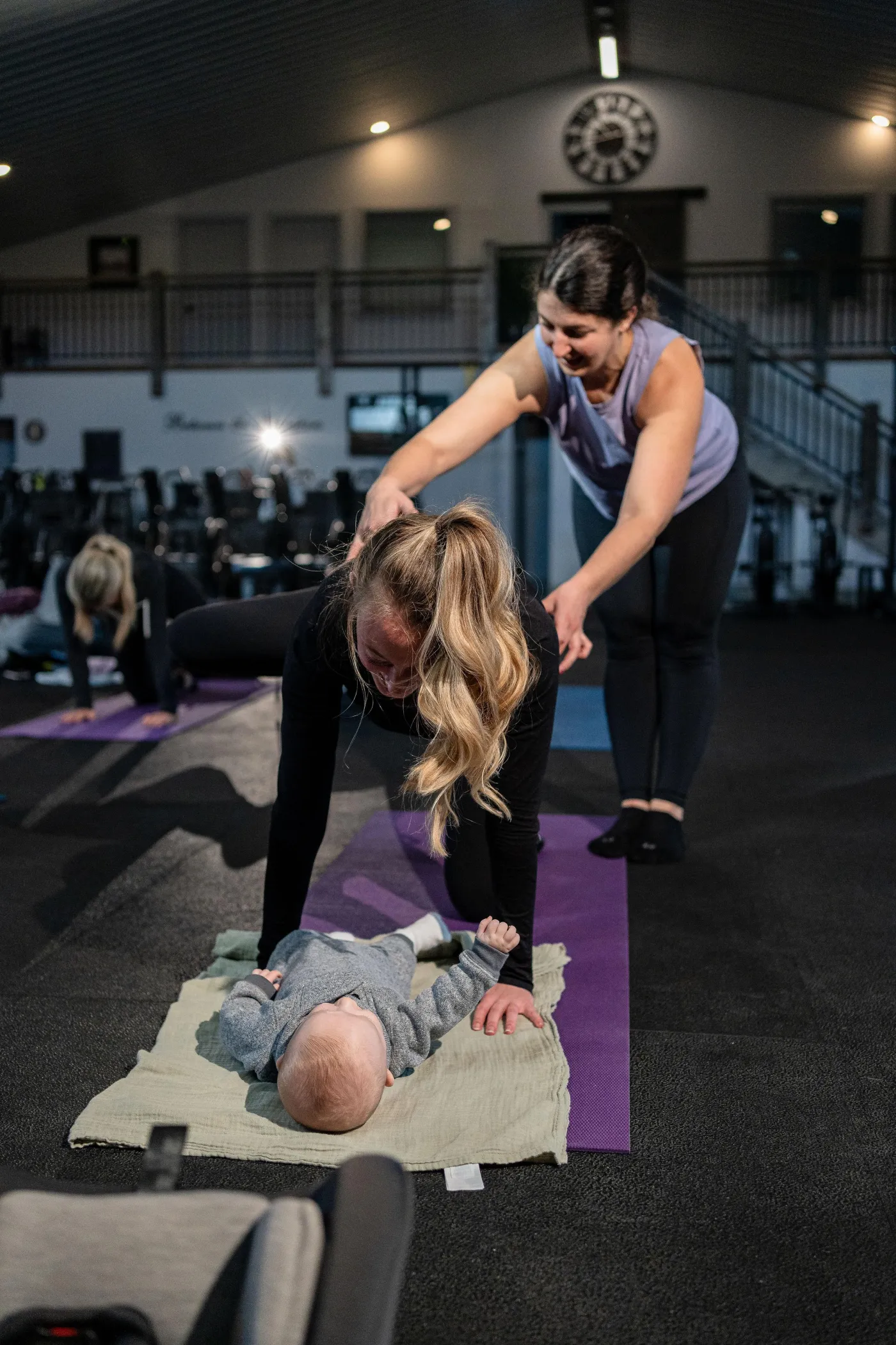 A Between The Bumpers coach helping a new mom train with her baby on the mat beside her
