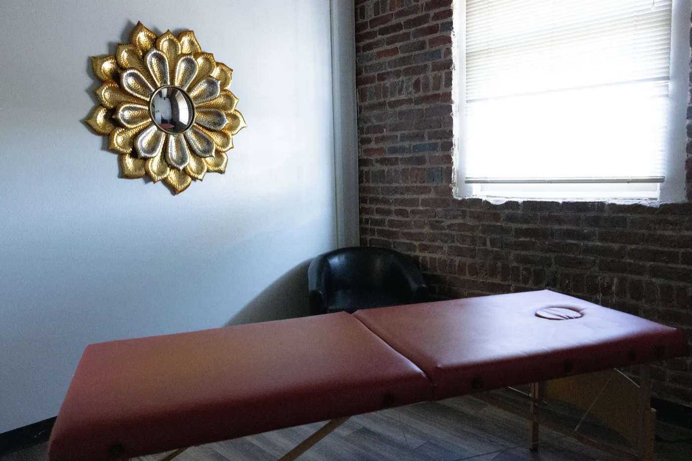 A Style City private suite with a brick wall, natural light, a gold mirror and a treatment table