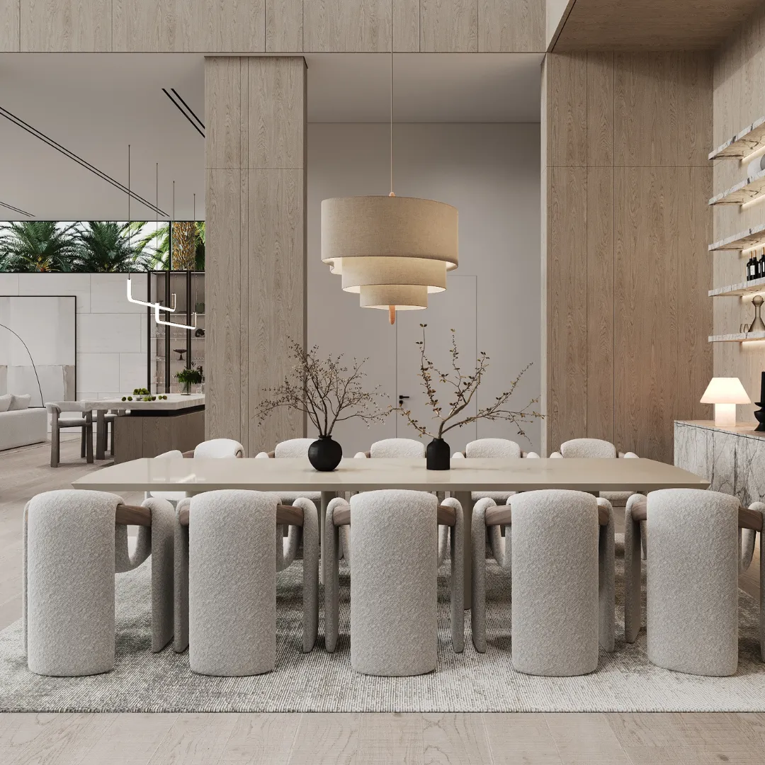 A dining room in warm wood and cream: a long table with upholstered chairs under a tiered pendant, the kitchen beyond