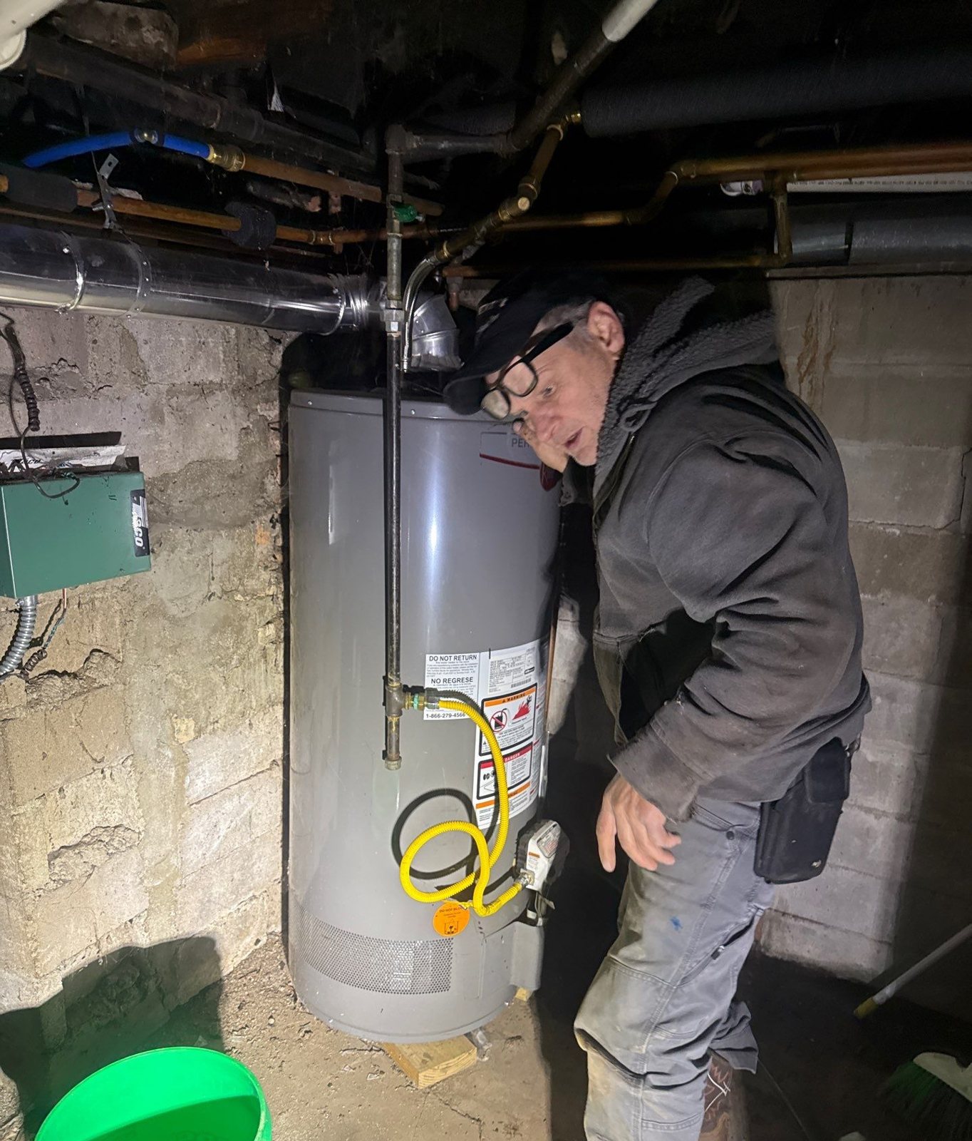 Repair King crew member at a basement water heater, draining lines into a bucket to winterize the plumbing