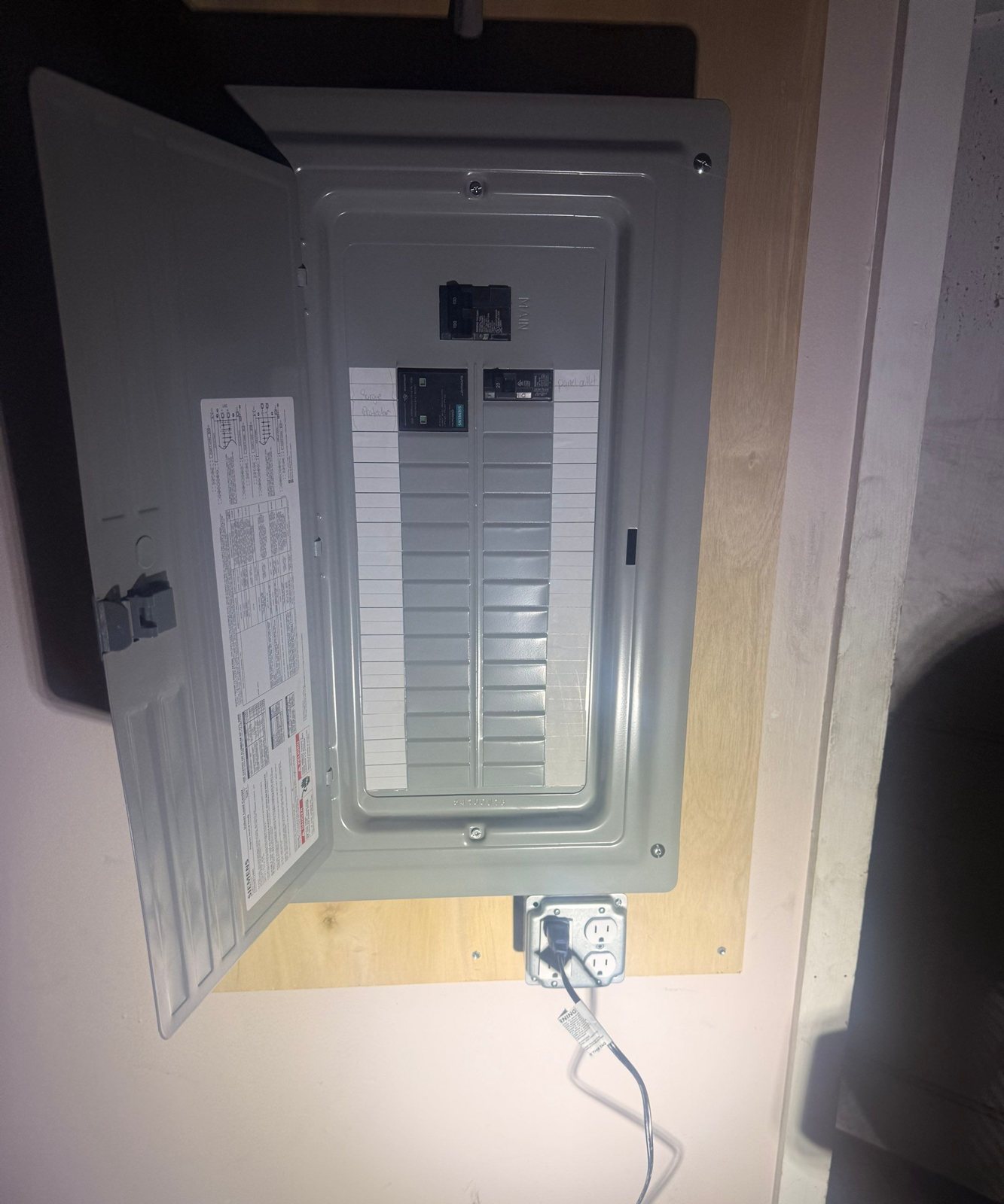 New electrical breaker panel mounted on a plywood backer with the cover open