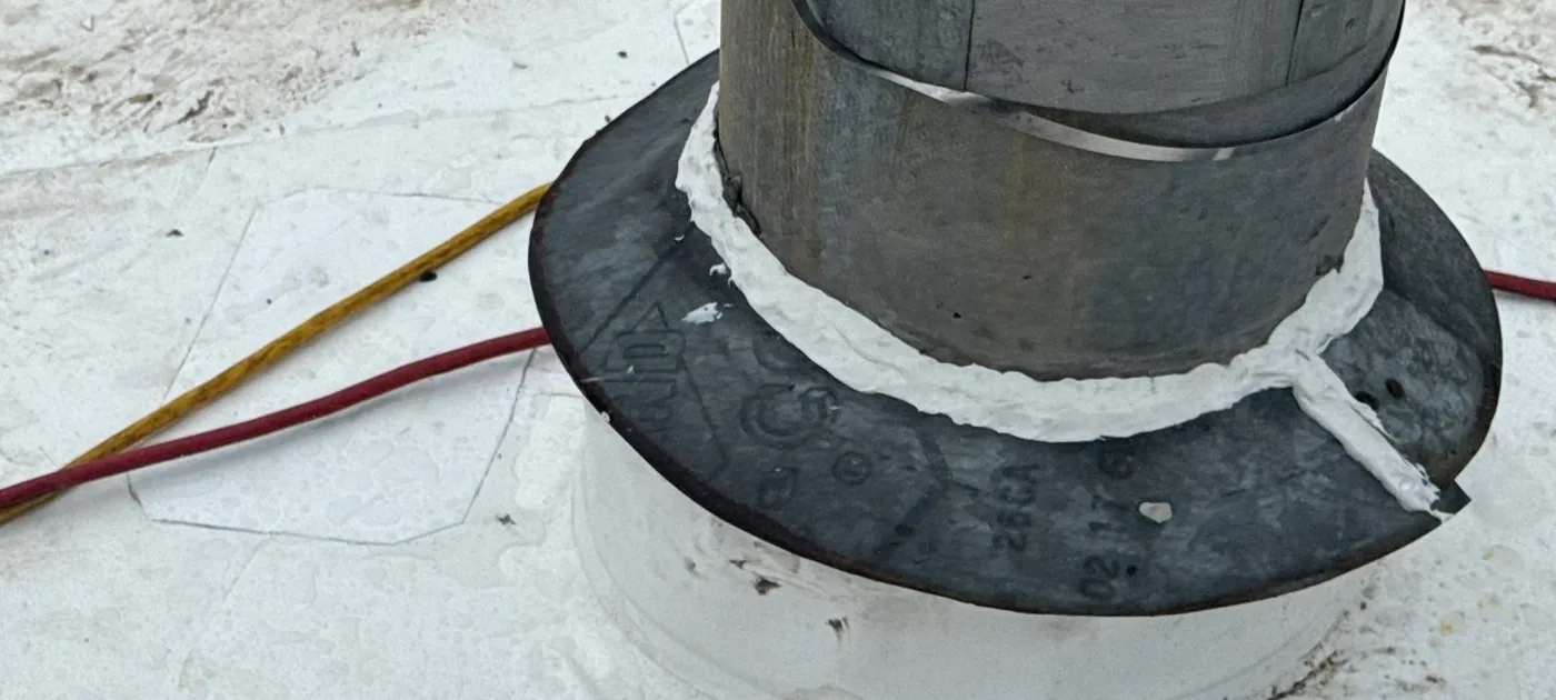 Metal flue pipe coming through a white membrane roof, with membrane flashed up around the base and a sealed metal storm collar above