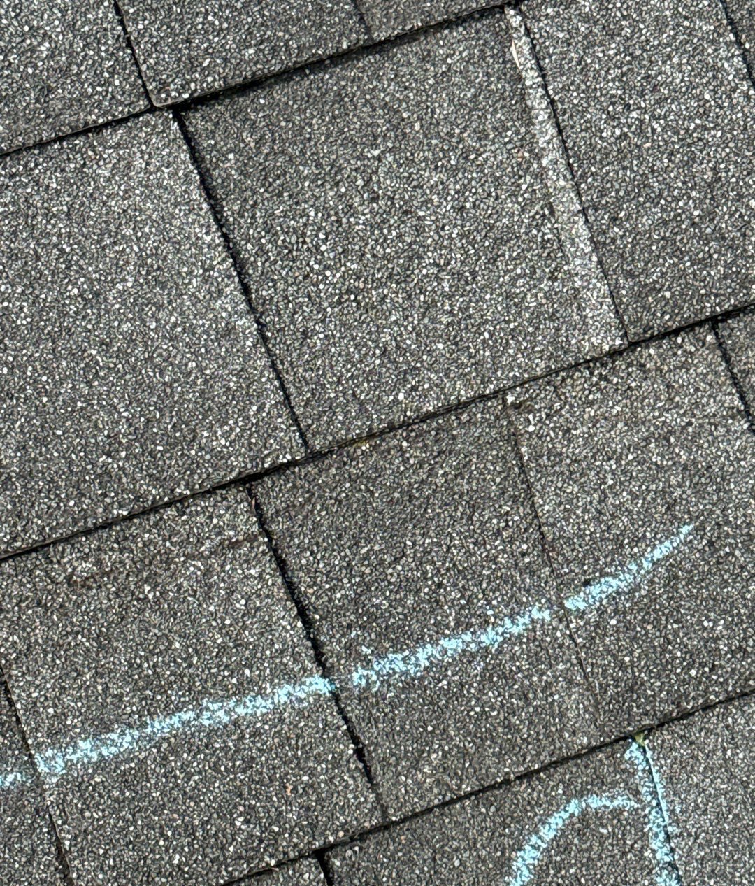 Gray architectural shingles with a blue chalk line underlining faint horizontal crease marks