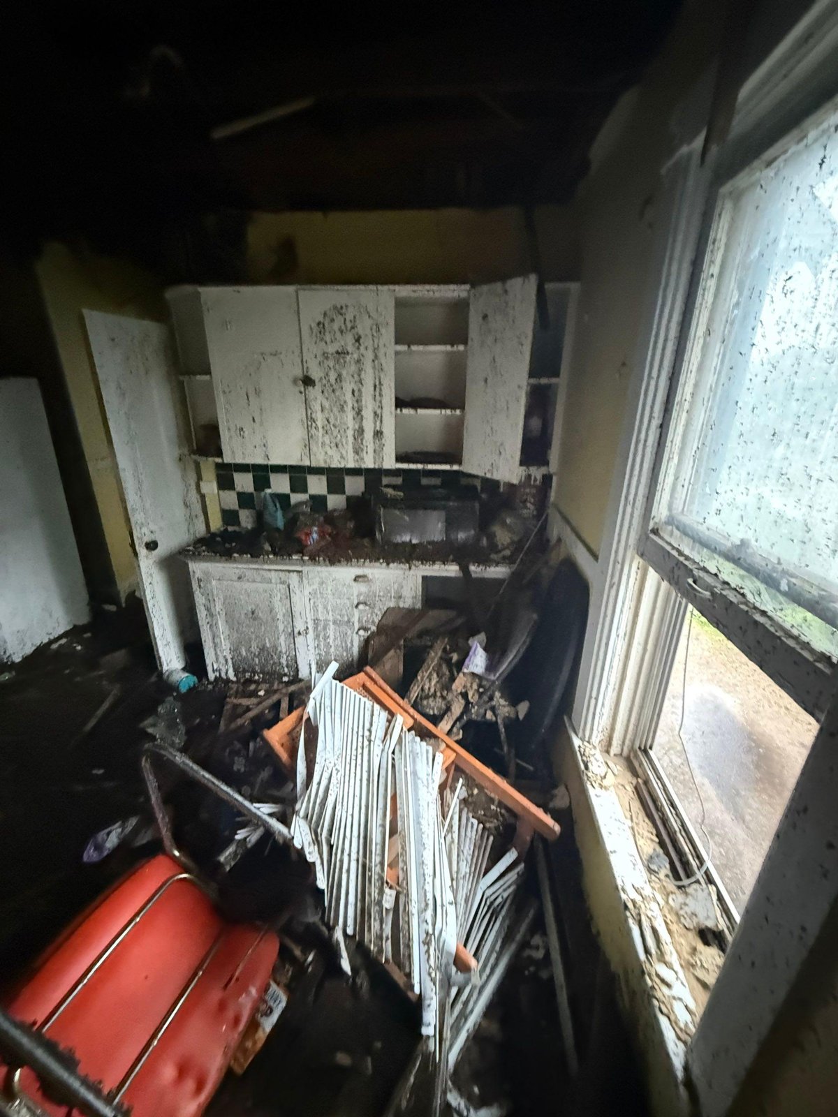 Fire-damaged kitchen with soot-covered cabinets, collapsed debris on the floor and a window coated in grime