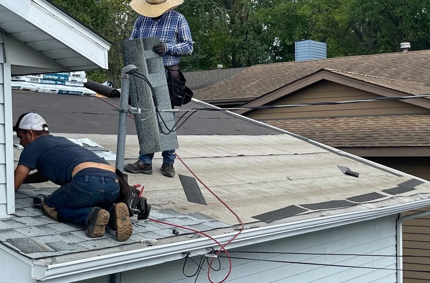 Two roofers on a St. Paul roof after tear-off, one kneeling at the eave edge and one carrying material