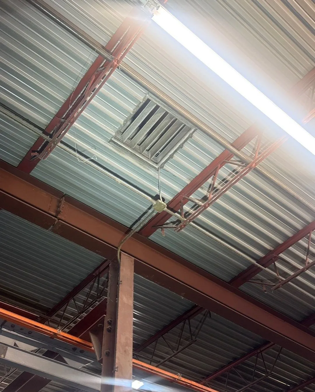 Underside of a corrugated steel roof deck resting on steel bar joists and a beam inside a commercial building