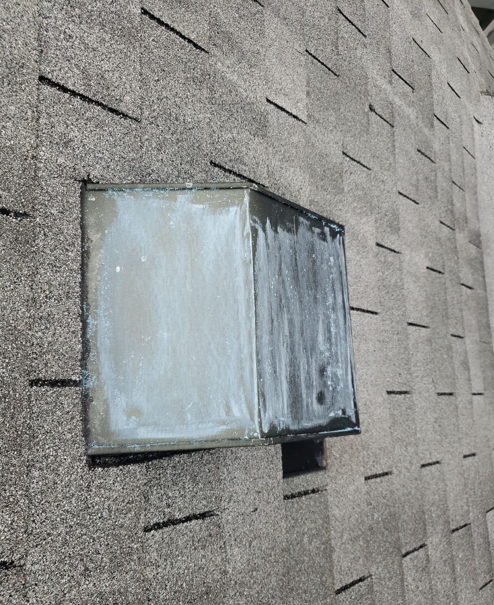 Square metal roof vent on asphalt shingles, smeared with white and gray sealant