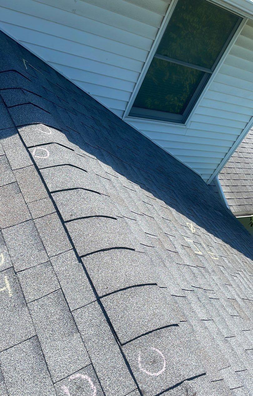 Ridge cap shingles along a roof peak with chalk circles marking impacts