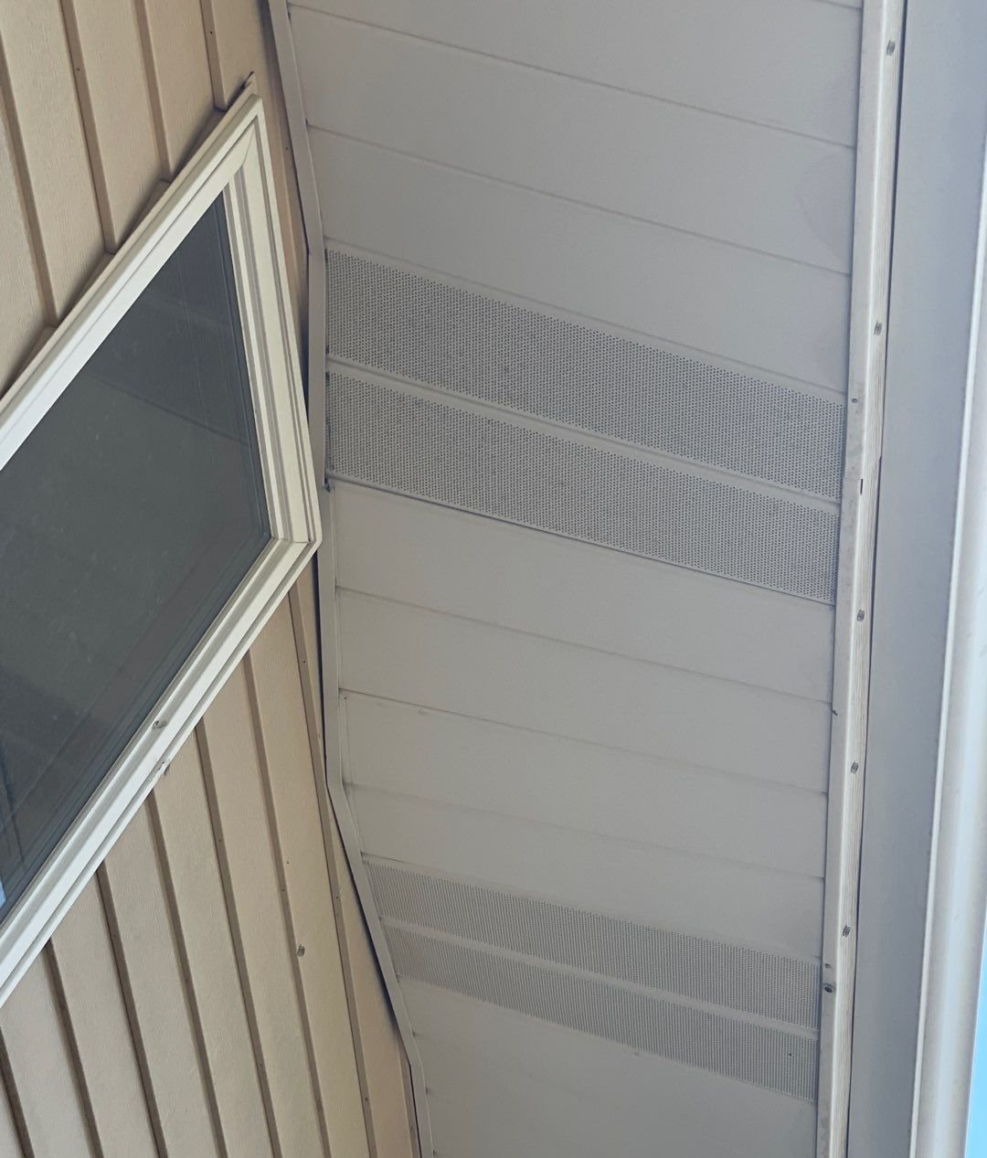 Perforated vented soffit panels under a roof overhang next to siding and a window