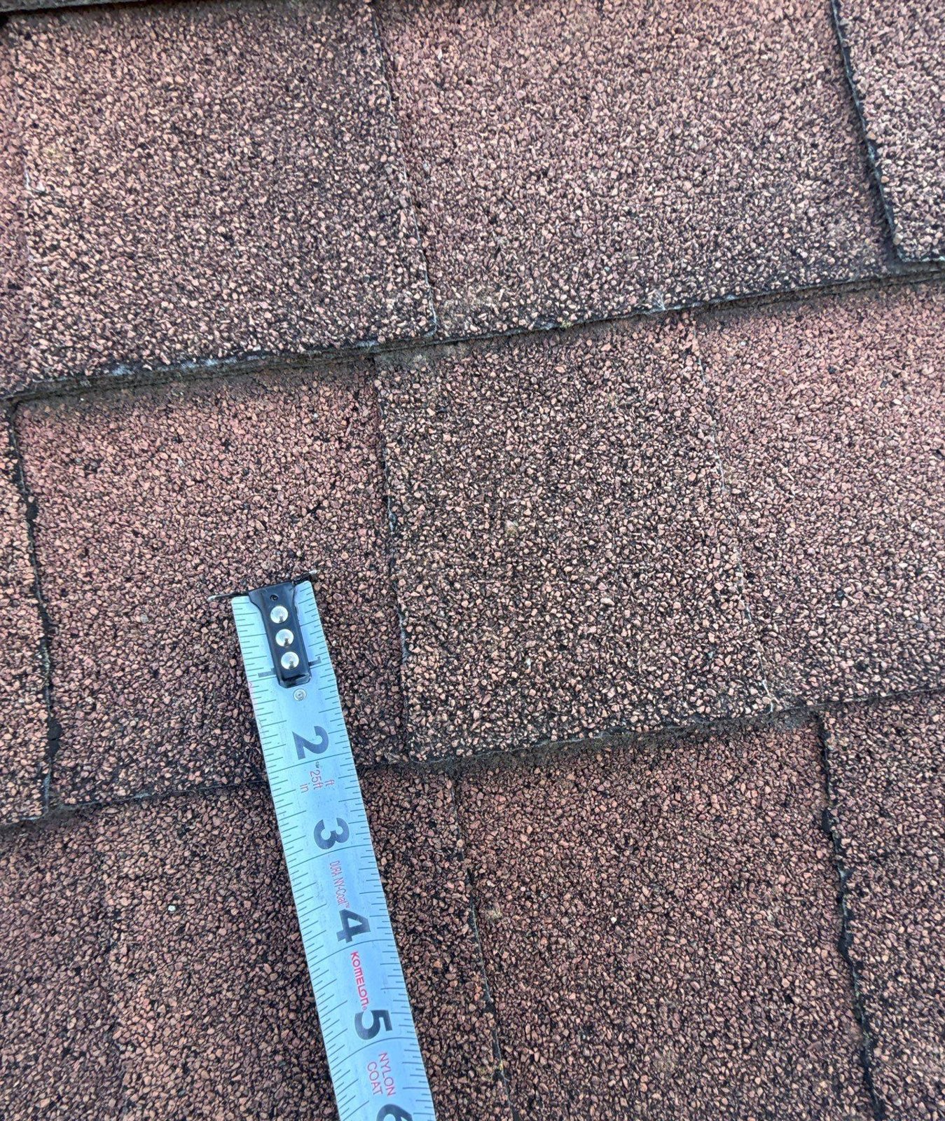 Tape measure laid across weathered brown shingles to show scale in an inspection photo