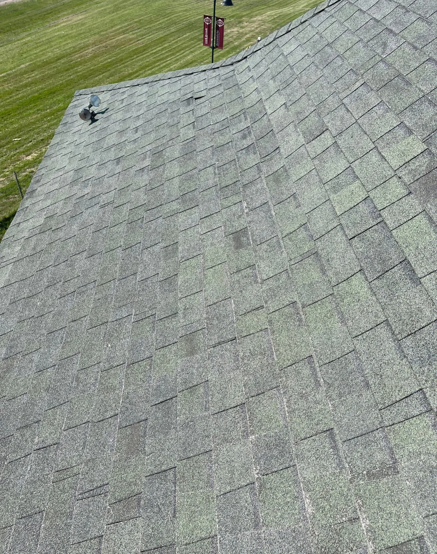 Wide view of a weathered gray-green asphalt shingle slope with blotchy, uneven color and thin-looking shingles