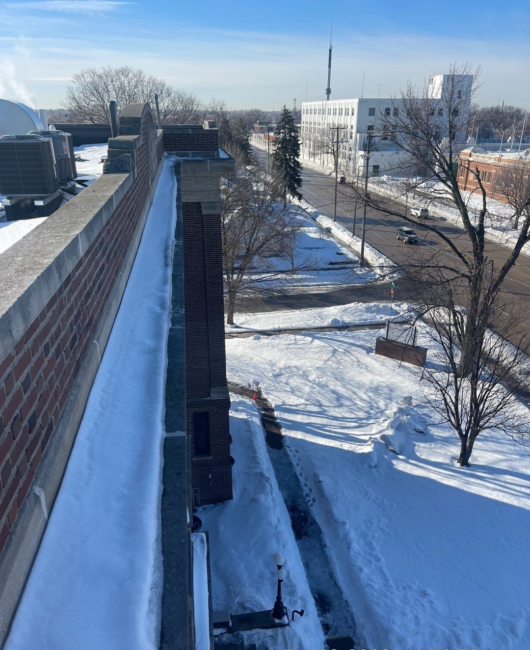 Narrow band of snow built up against a tall brick parapet on a flat roof, with rooftop units beyond