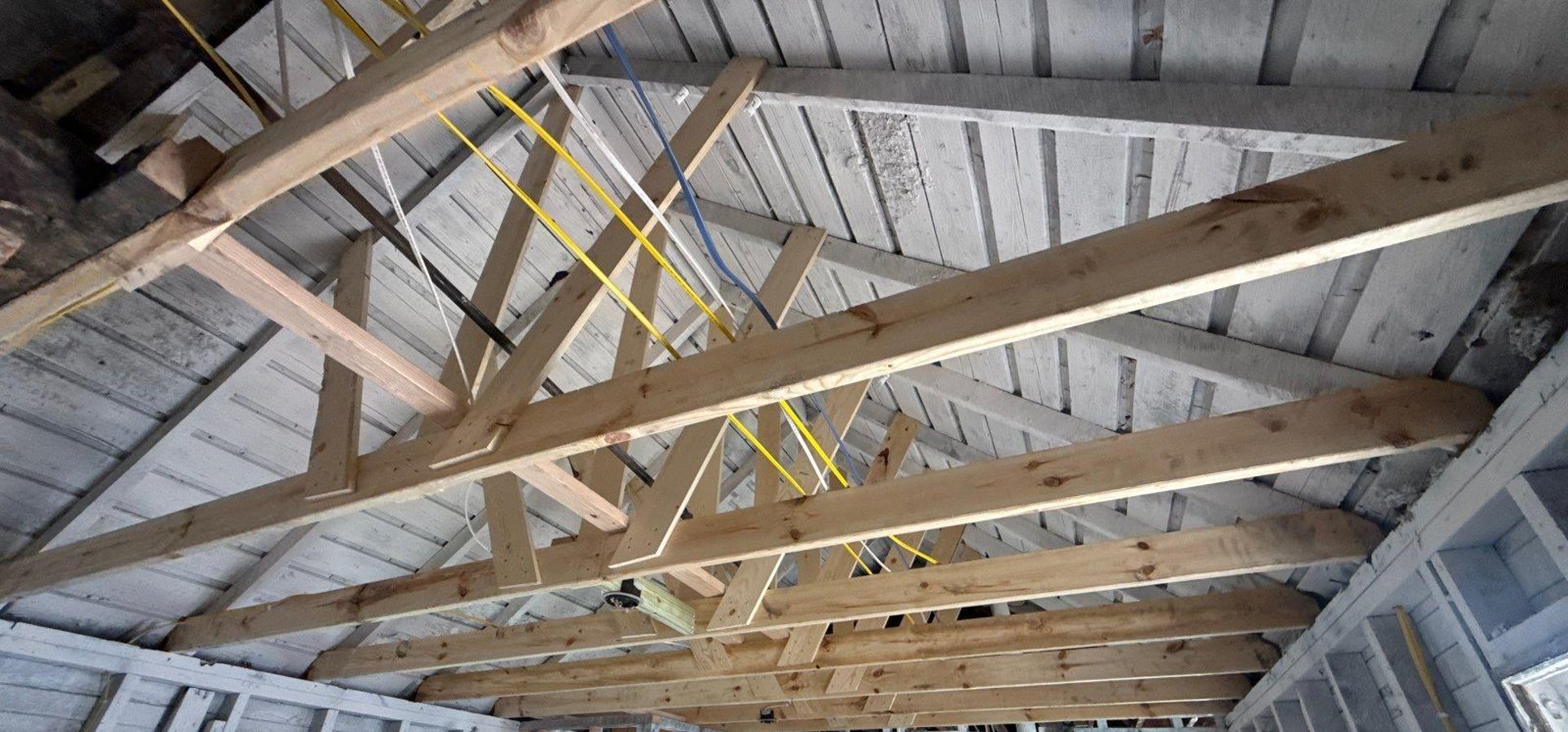 New lumber rafters and ties sistered into an old roof structure above freshly framed interior walls