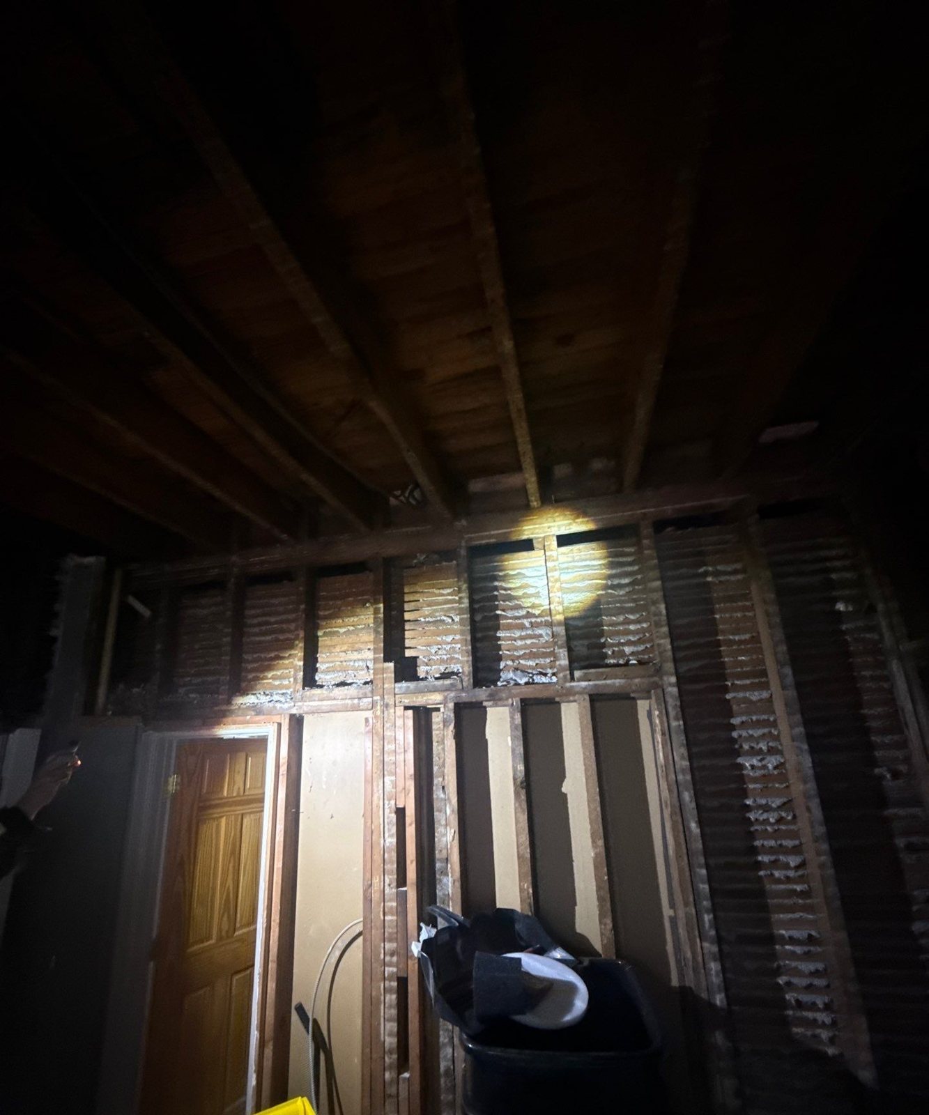 Dark open wall and ceiling cavity in an older house showing continuous framing between floors