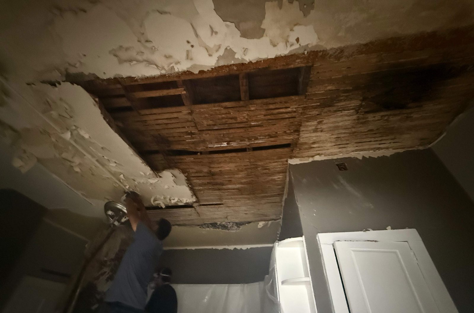 Kitchen ceiling drywall removed, exposing the joists above as a worker continues demolition