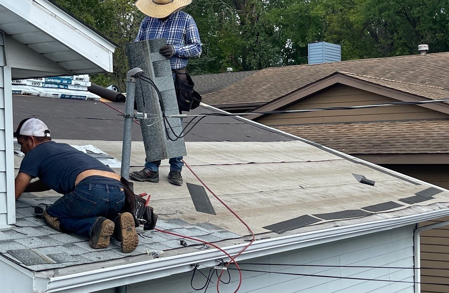 Two roofers installing new asphalt shingles over fresh underlayment on a St Paul house
