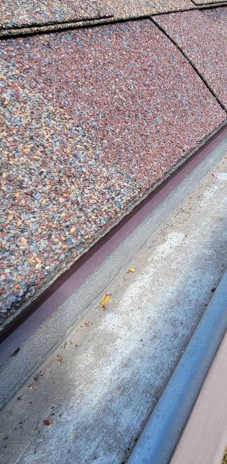 Looking down a gutter along a worn shingle roof edge, with shingle granules collected in the trough