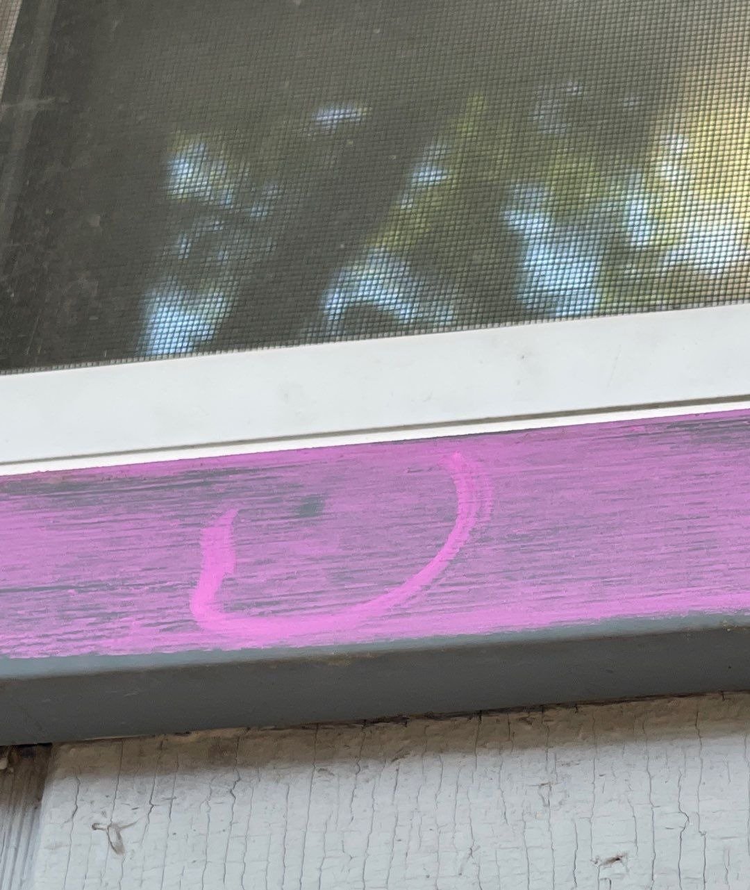 A hail dent circled in pink chalk on the metal wrap below a window screen