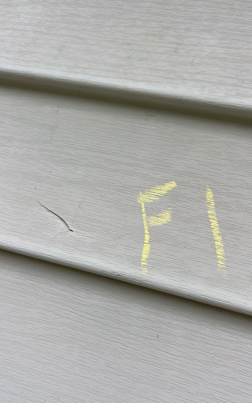Light-colored vinyl siding panel with a short crack next to the chalk label F1