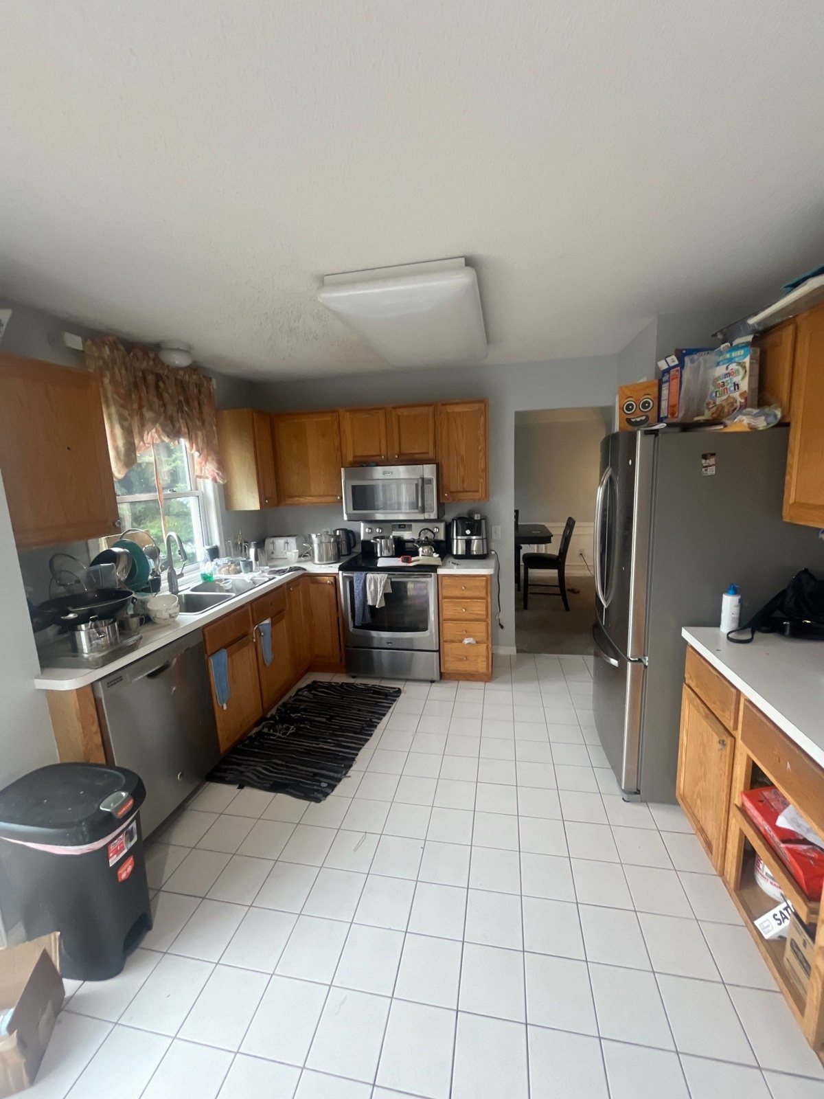 Galley-style kitchen with oak cabinets, stainless refrigerator, and white tile floor