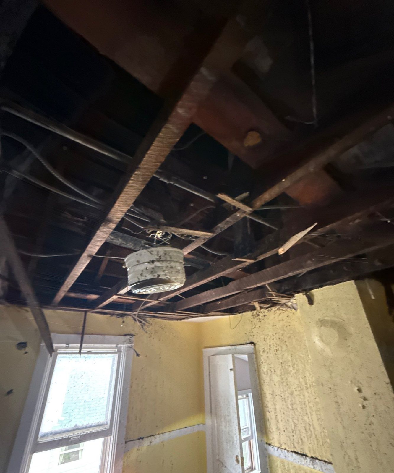 Collapsed plaster ceiling exposing wood lath and joists above a room with two windows