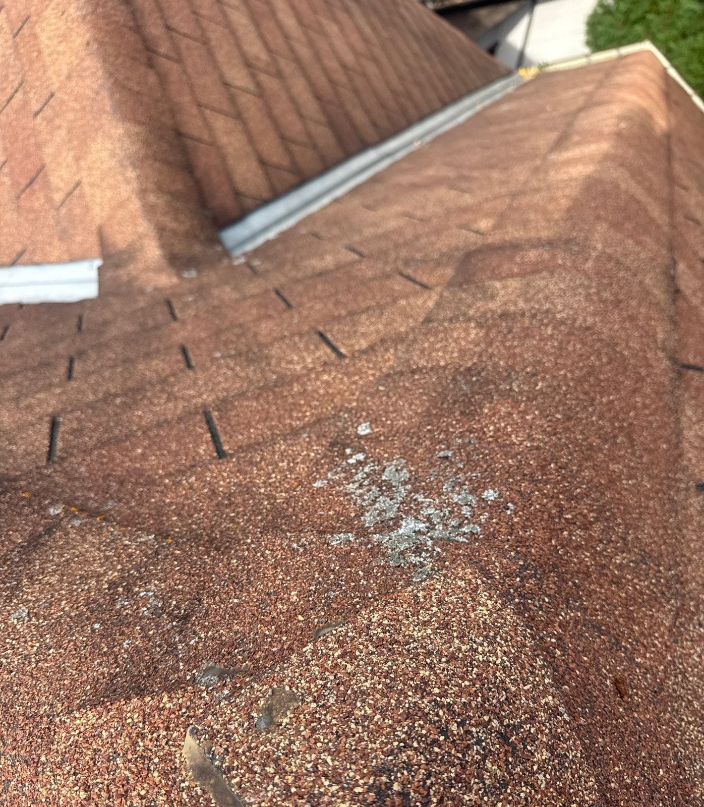 Worn asphalt shingles with lichen growth and granule loss near a ridge
