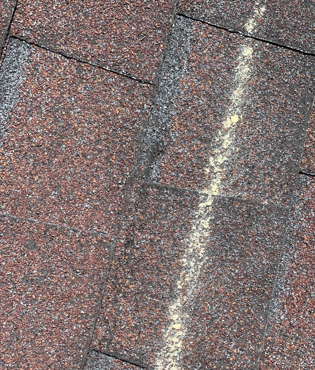 Red-brown shingles with a white chalk line drawn parallel to a wind crease across the tabs
