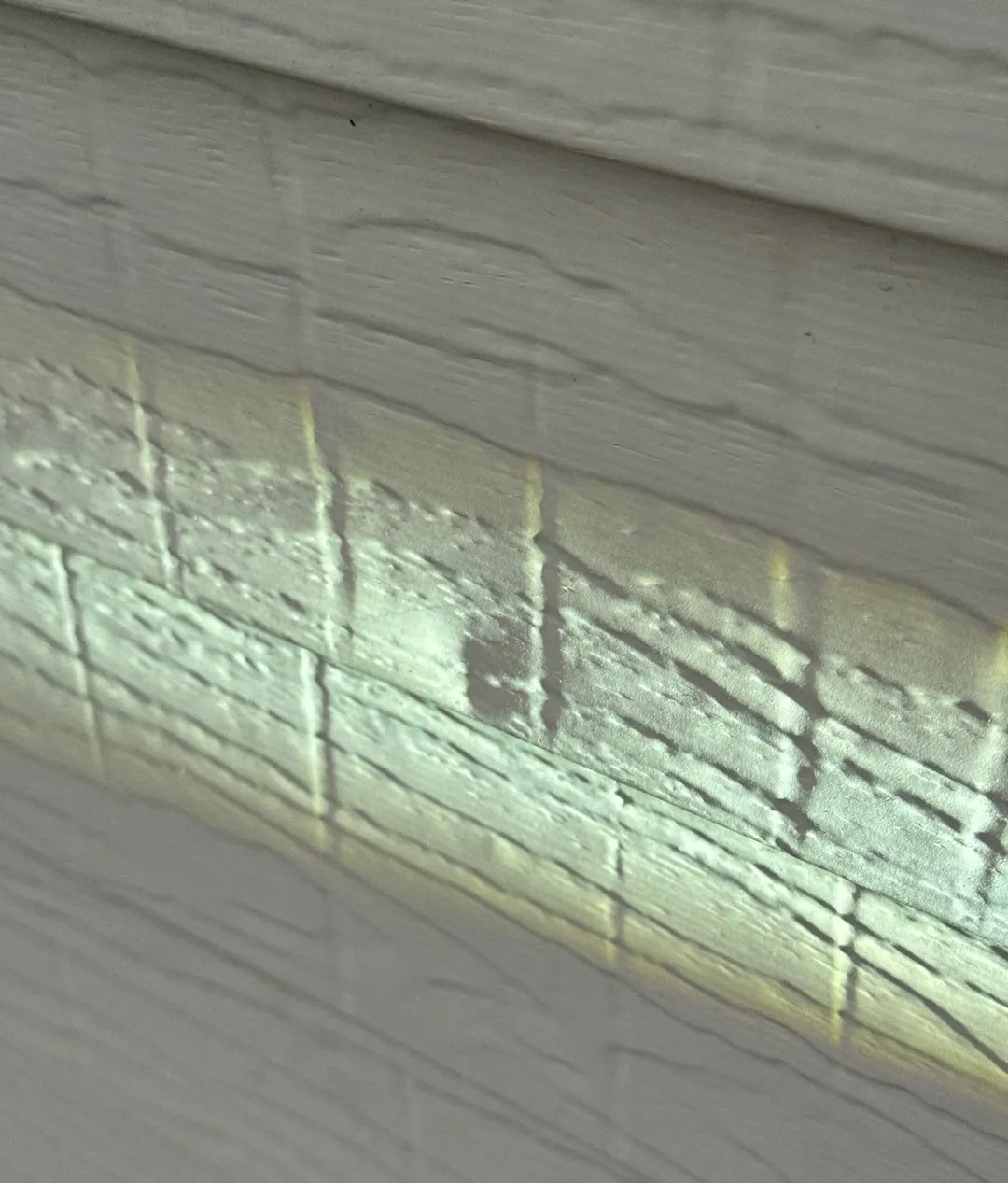 Light-colored siding lit from the side with a flashlight, showing small dents along the lap