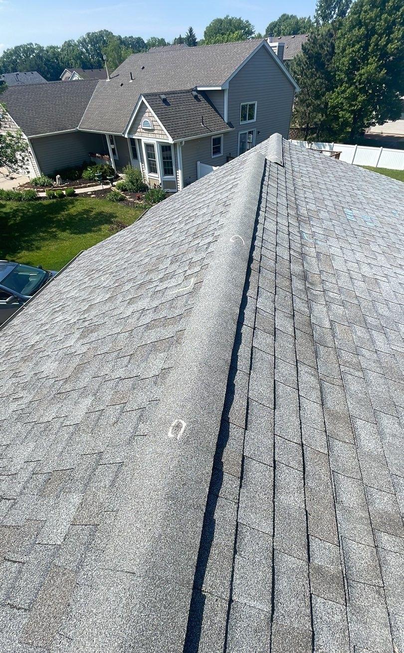 Ridge cap shingles running along the peak of a gray shingle roof with a chalk circle marking an impact