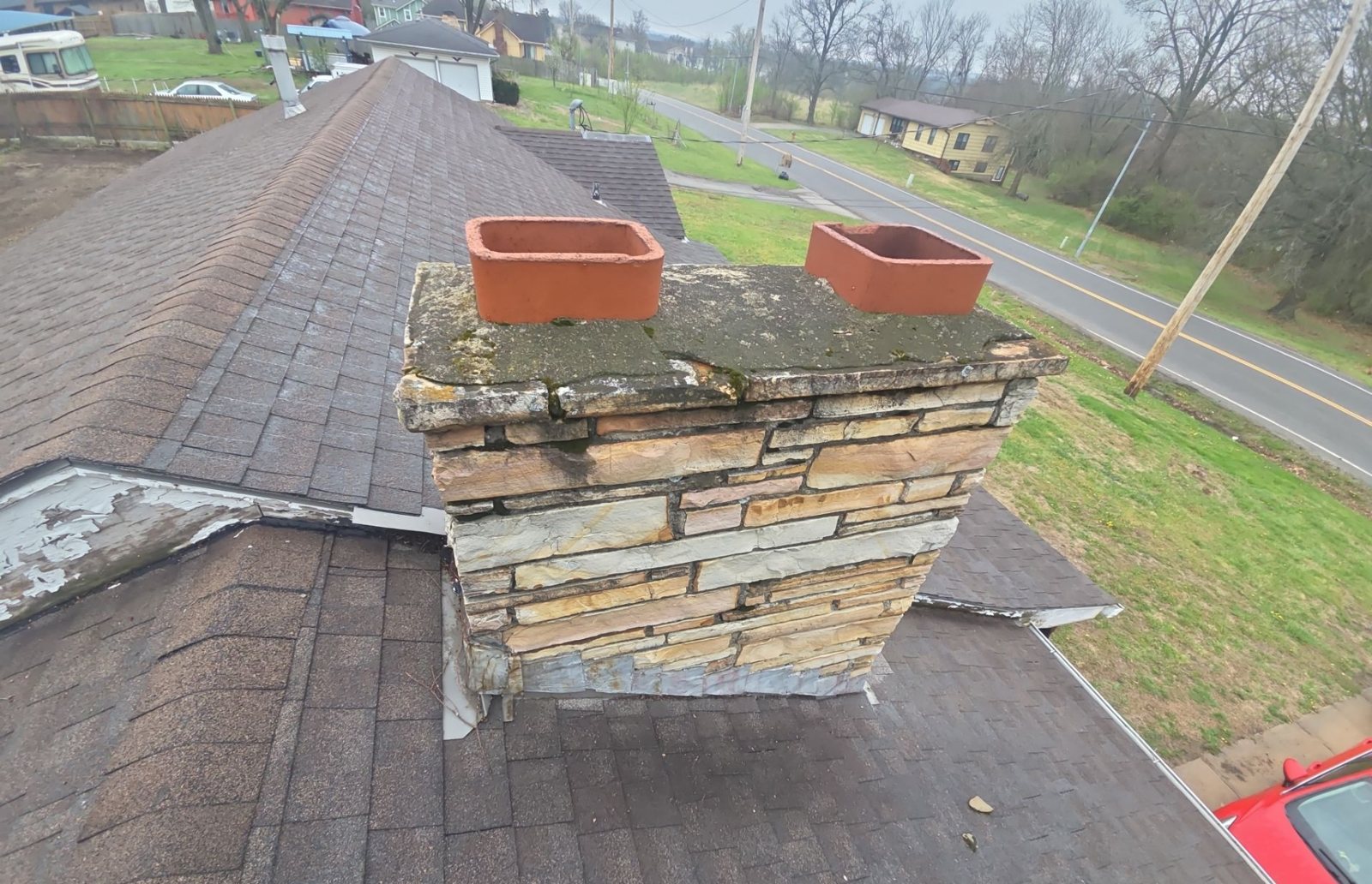 Weathered stone and brick chimney with clay flue tiles on an asphalt shingle roof