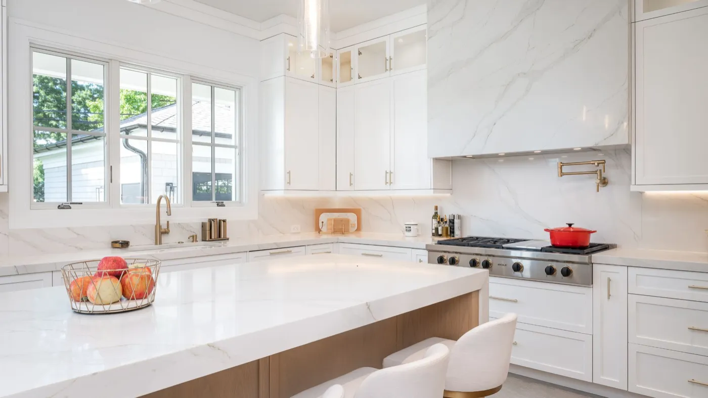 The same kitchen finished: white cabinetry, marble counters and backsplash, brass fittings and a range under the marble hood