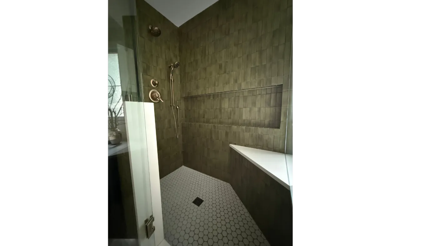 Inside a walk-in shower with a built-in bench, olive vertical tile, and a hexagon tile floor