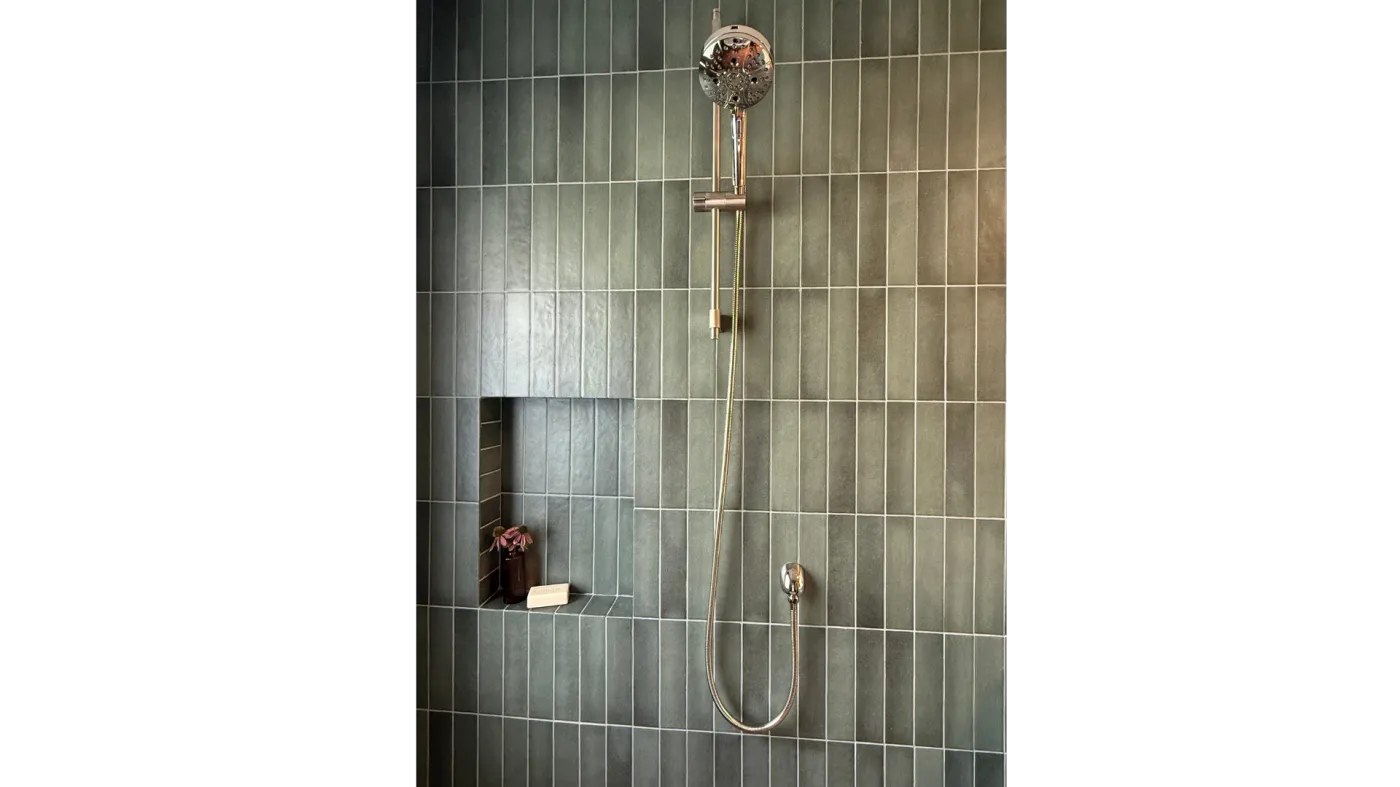 Polished shower fixture and handheld sprayer on green matte vertical tile with a recessed niche