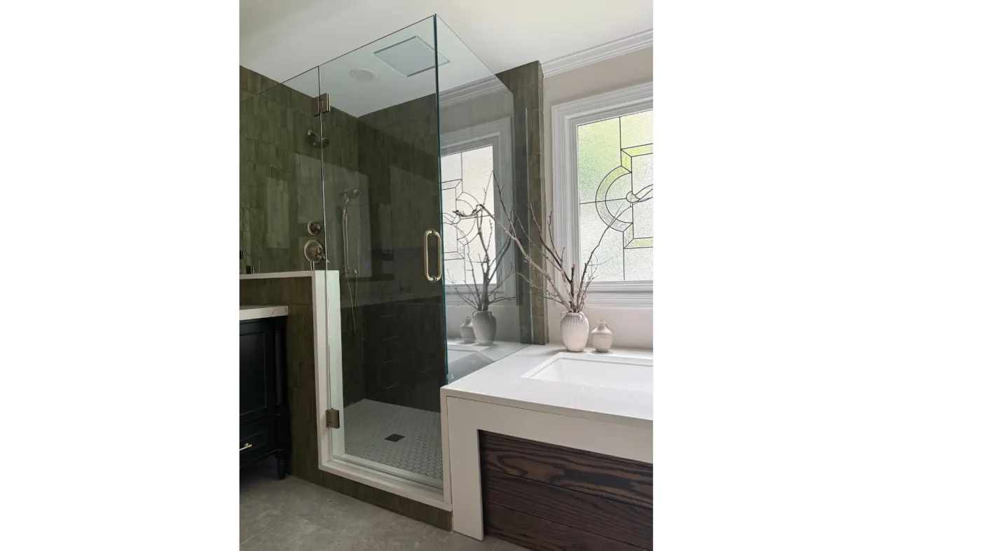 Frameless glass walk-in shower enclosure with olive vertical tile and a stained glass window in an Atlanta primary bath