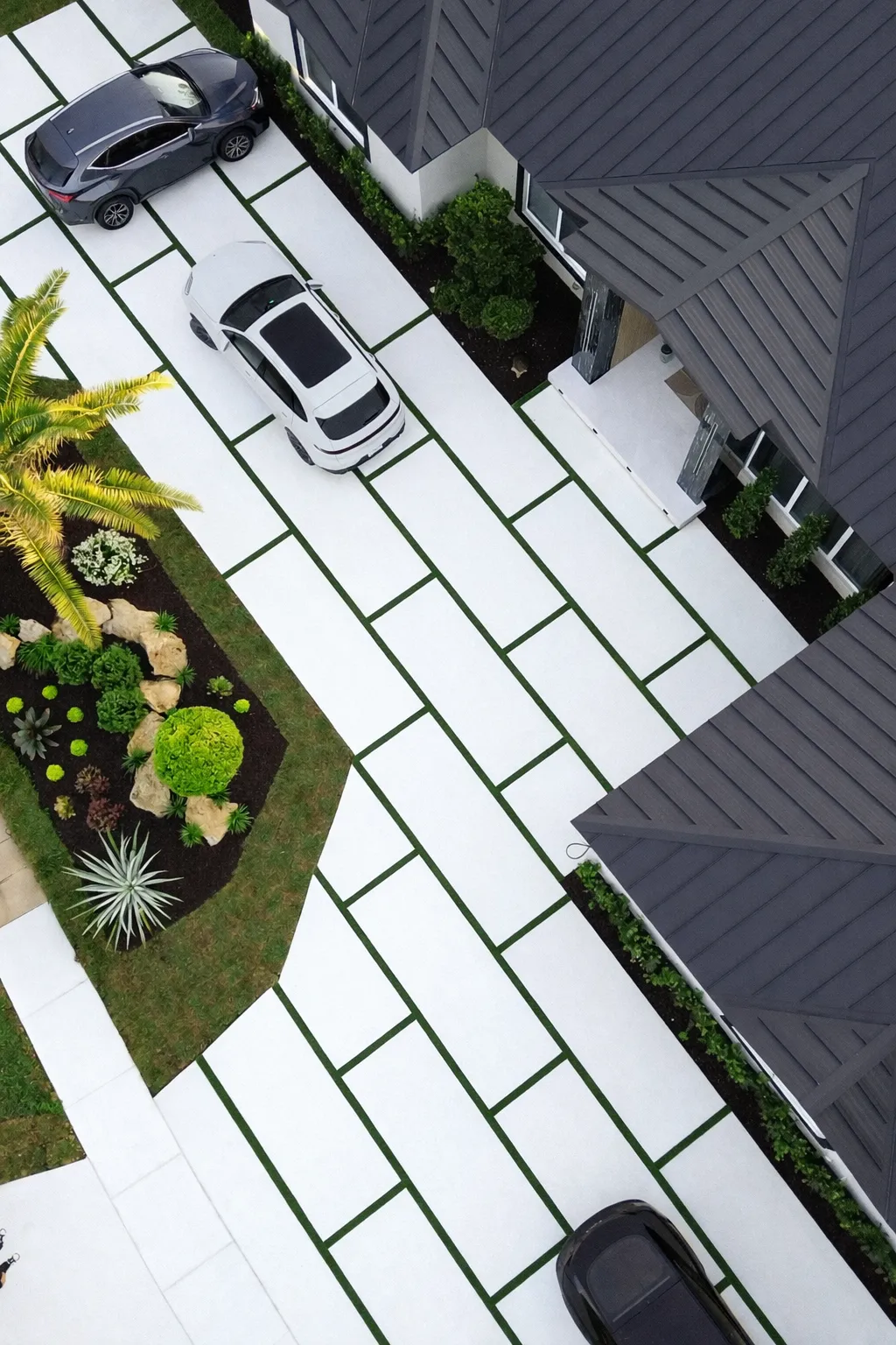 Aerial view of modern white concrete driveway with green turf strips installed by Concrete Designs LLC in South Florida