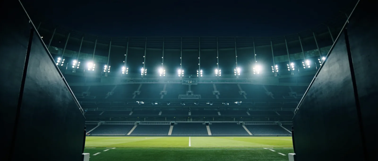 Empty stadium at night under floodlights, seen from the players' tunnel