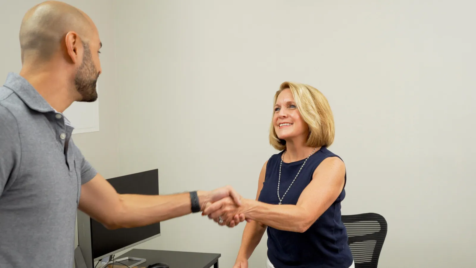 A roofing contractor shaking hands with an insurance agent in the agent's office