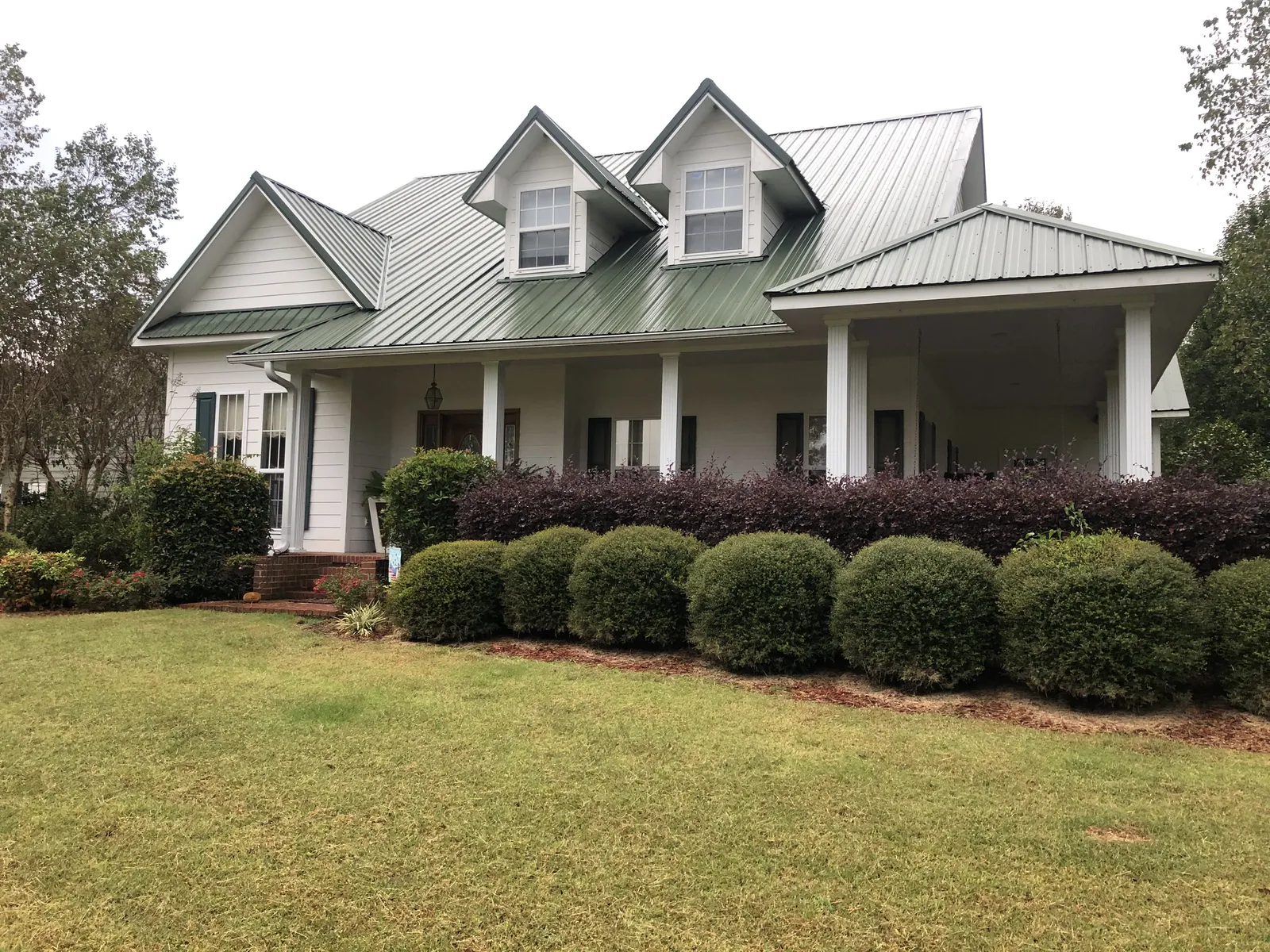 White farmhouse with a green standing-seam metal roof, dormers and a covered front porch