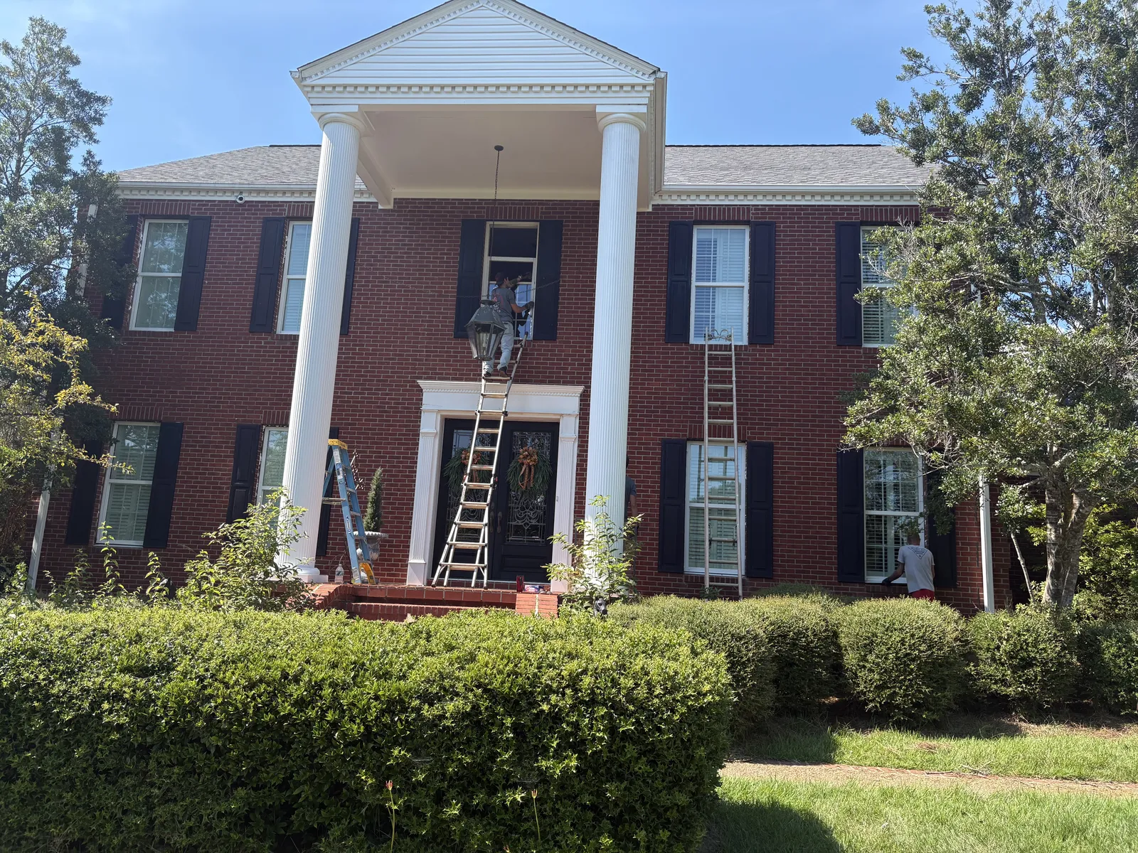 Window replacement in progress on a brick two-story home with white columns