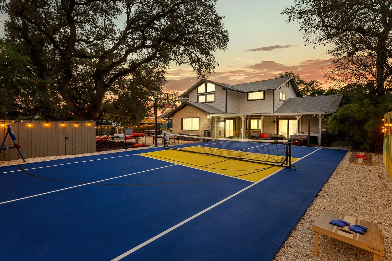 Multi-use court in blue and gold behind a modern farmhouse at dusk