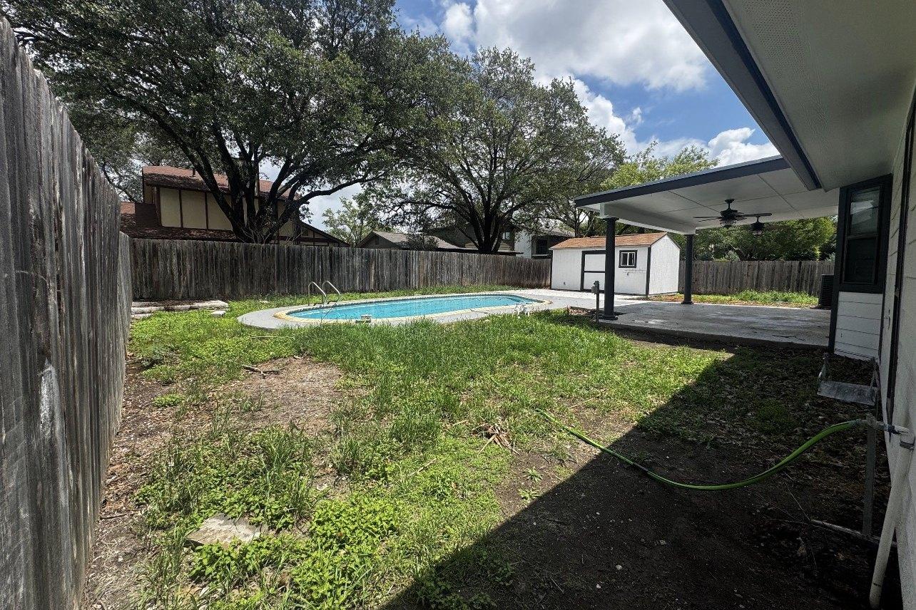 Backyard before: overgrown lawn around an existing pool, bare concrete patio under a covered porch