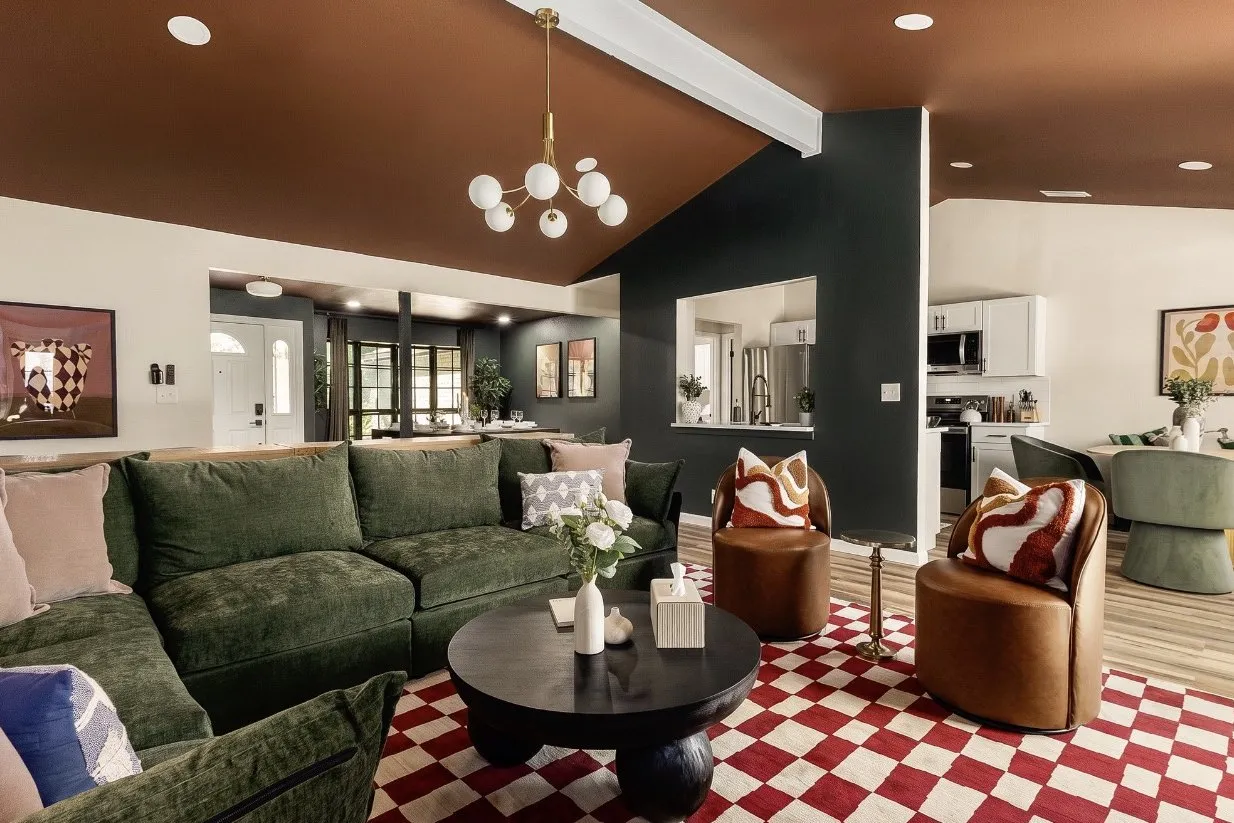 Living room finished: painted vaulted ceiling, green sectional, dark feature wall and a checkered rug