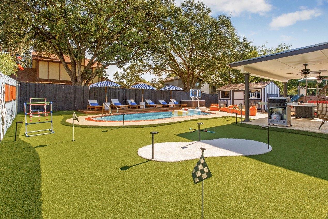Backyard after: turf, putting green, striped umbrellas and loungers around the same pool, covered patio with ceiling fans