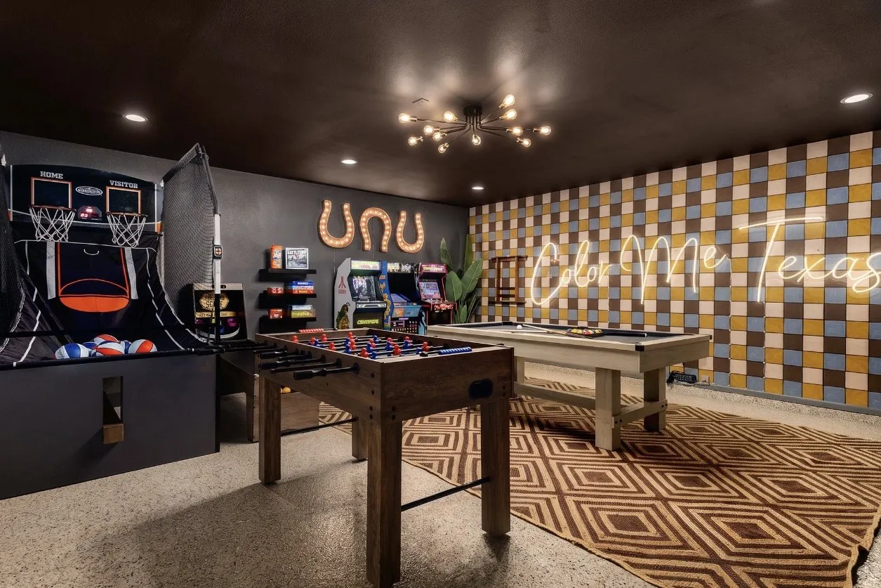 Game room after: pool table, foosball, arcade cabinets, a checkered feature wall and a neon sign in the former garage