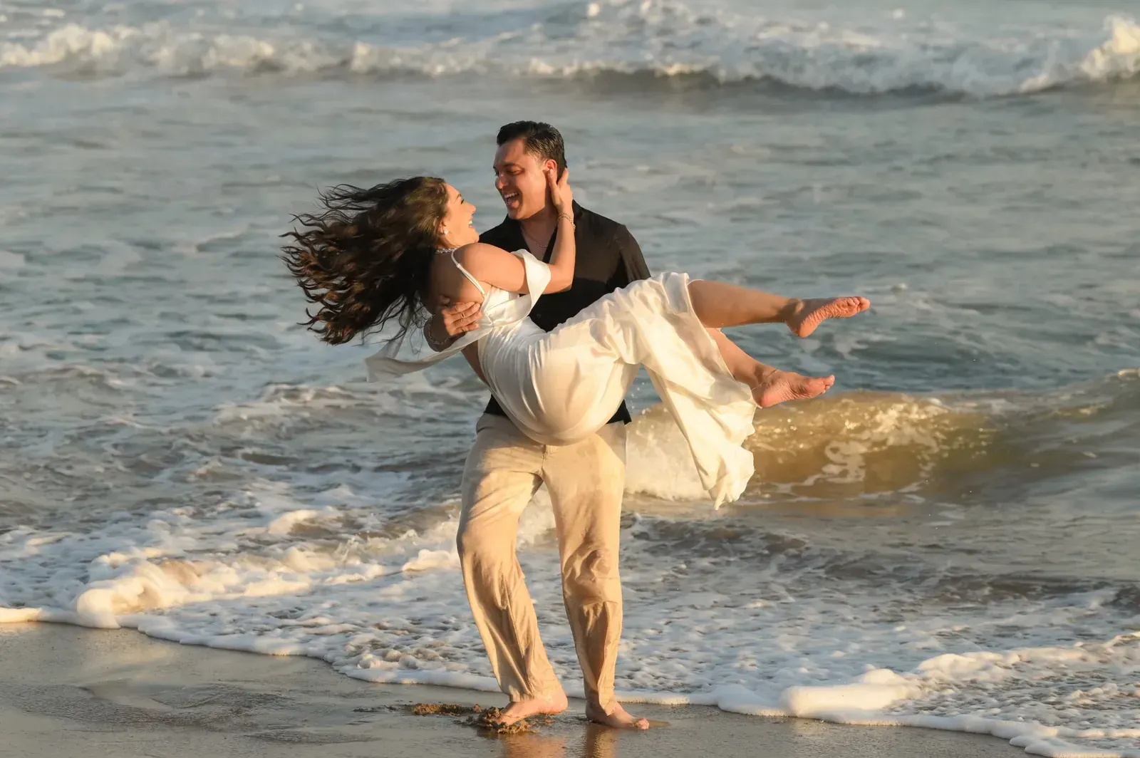 Brian carga a Isamar entre las olas; los dos ríen
