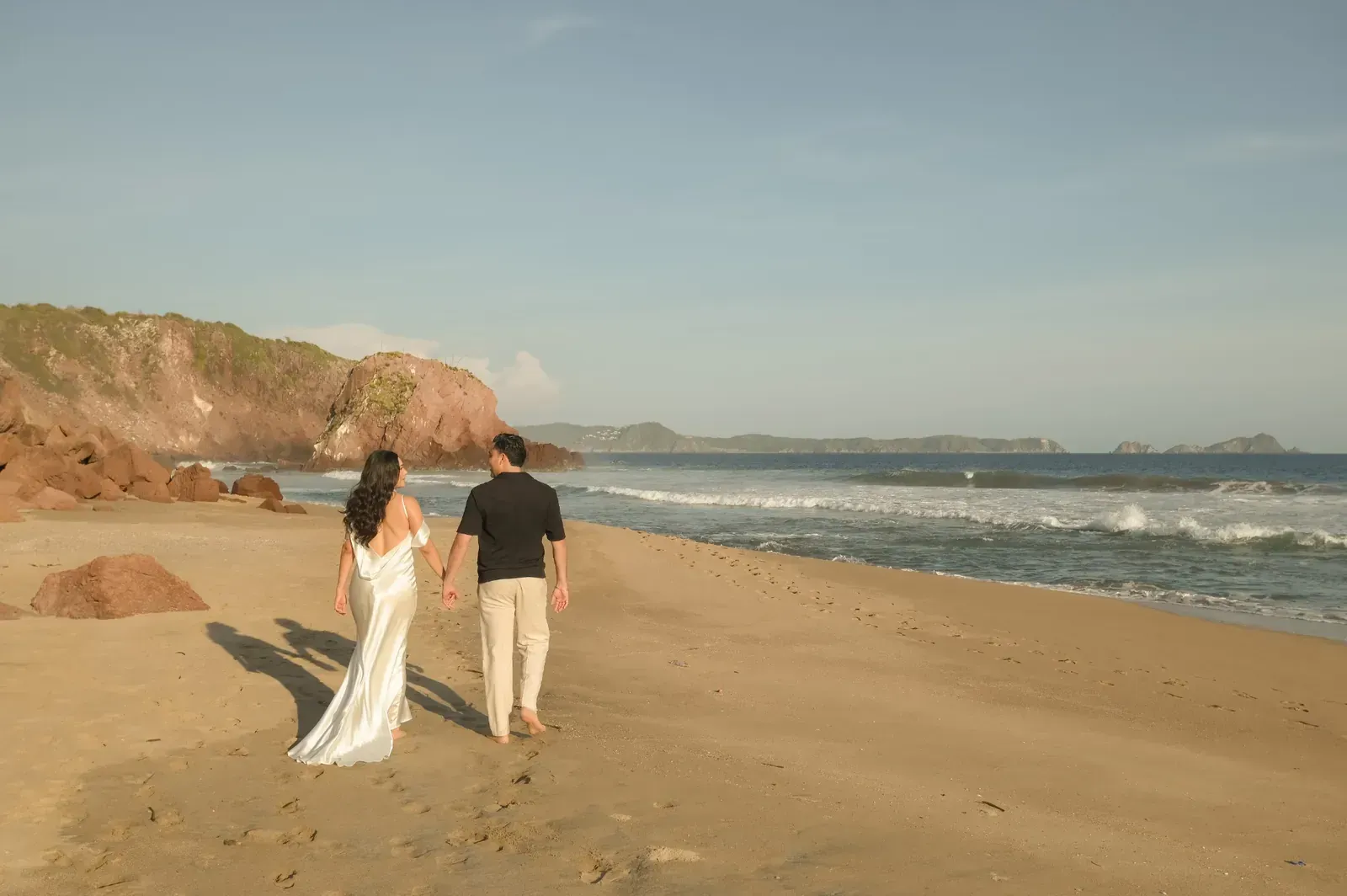 Isamar y Brian caminan por la playa, de espaldas