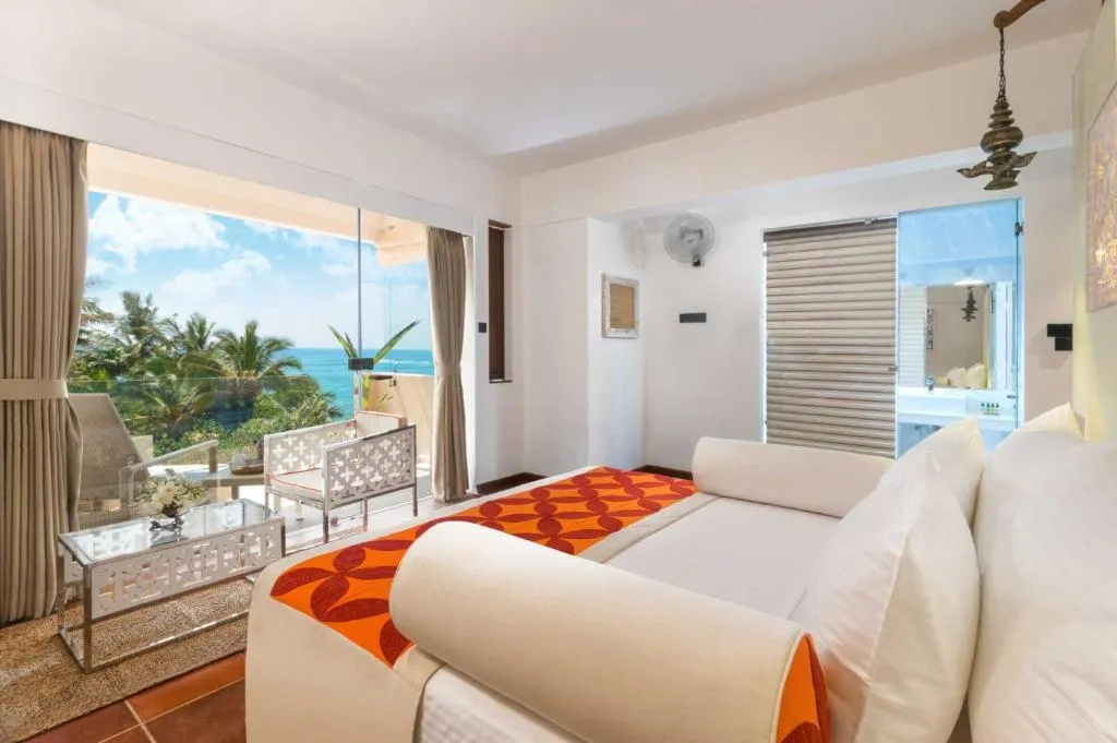 Ocean-view guest room at Ayurvie Weligama with a private balcony overlooking palm trees and the Indian Ocean.
