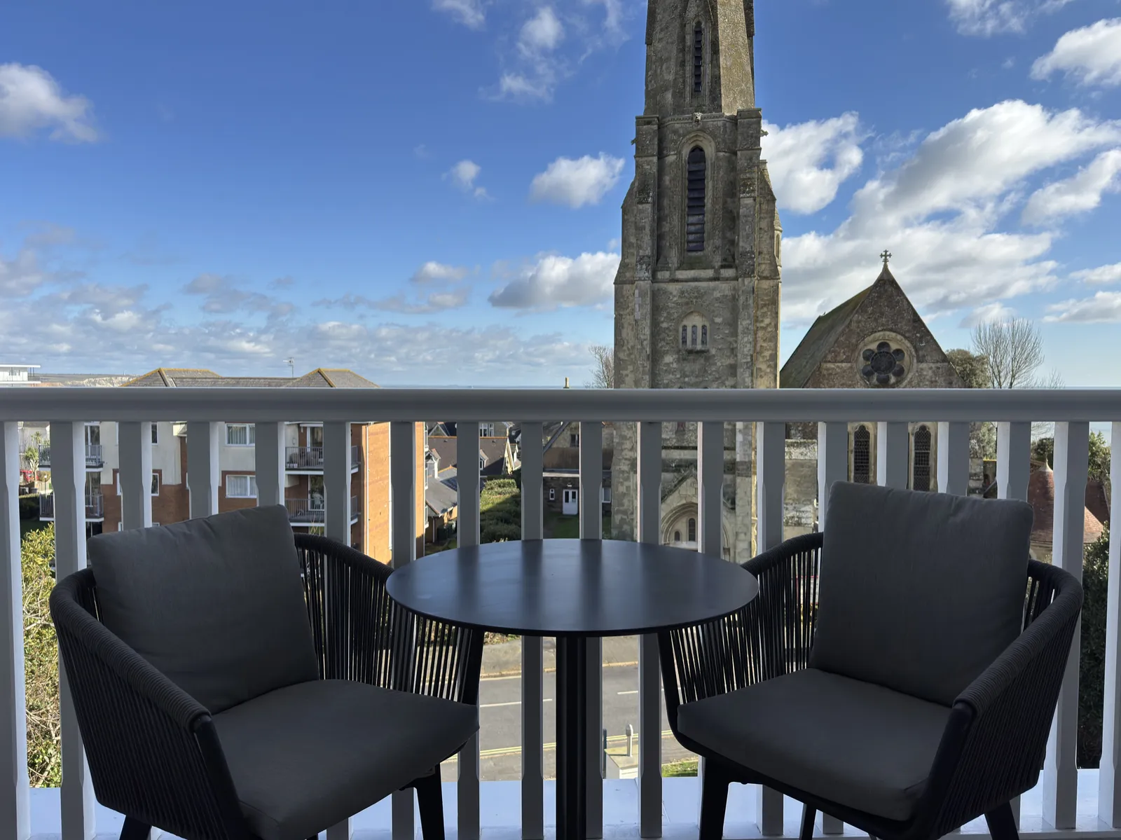 Private balcony with two chairs, a table and a church spire against blue sky at The Fig Tree, Shanklin