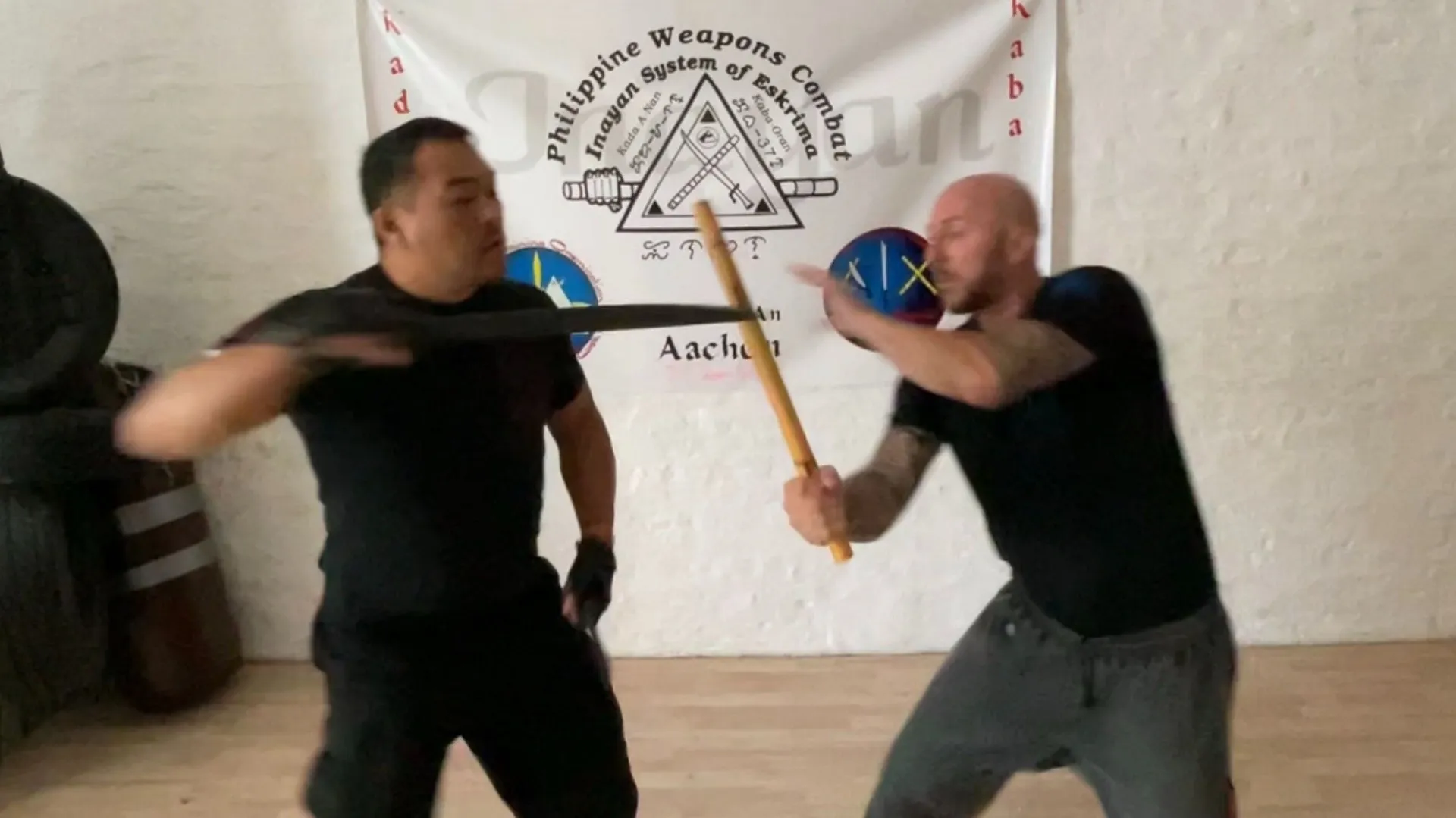 Stick and blade training in front of an Inayan System of Eskrima banner