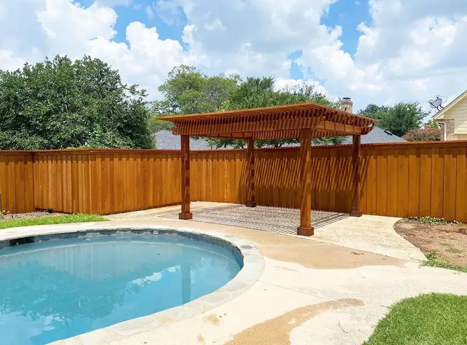 Cedar pergola beside a backyard pool with a stained board-on-board fence